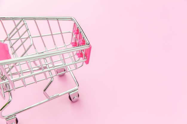 Piccolo supermercato carrello di spesa per lo shopping giocattolo con ruote isolato su rosa pastello colorato tr...