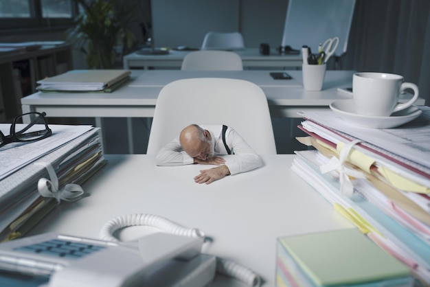 Piccolo uomo d'affari che dorme alla sua scrivania