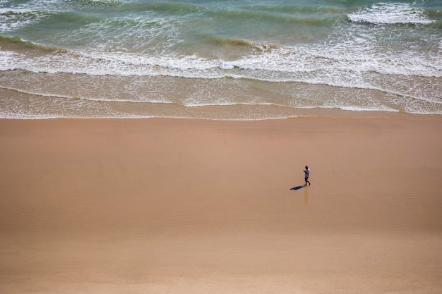 Piccolo uomo solo che guarda il cellulare su una spiaggia con molto spazio per le copie