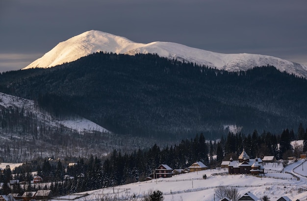 Piccolo villaggio alpino e montagne innevate invernali alla prima luce solare dell'alba intorno a Voronenko Carpazi Ucraina