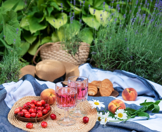 Picnic all'aperto nei campi di lavanda. Vino rosato in un bicchiere, ciliegie e cappello di paglia sulla coperta