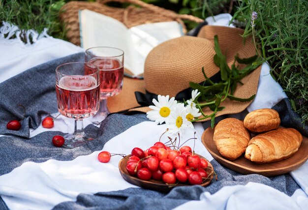 Picnic all'aperto nei campi di lavanda. Vino rosato in un bicchiere, ciliegie e cappello di paglia sulla coperta