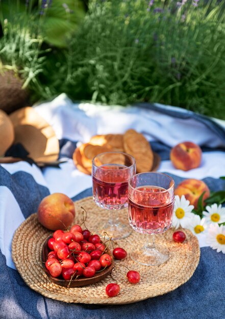 Picnic all'aperto nei campi di lavanda. Vino rosato in un bicchiere, ciliegie e cappello di paglia sulla coperta