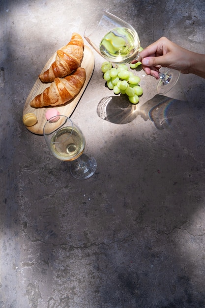 Picnic con vino bianco e croissant, qualcuno che tiene in mano il bicchiere, copia spazio sul tavolo, sovrapposizione di ombre