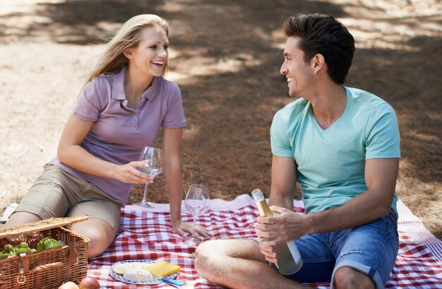 Picnic di coppia e bicchiere di vino in natura con celebrazione d'amore e data estiva o romanticismo per il giorno di San Valentino Giovani con cibo frutta e bottiglia di champagne nel bosco o nella foresta per l'anniversario