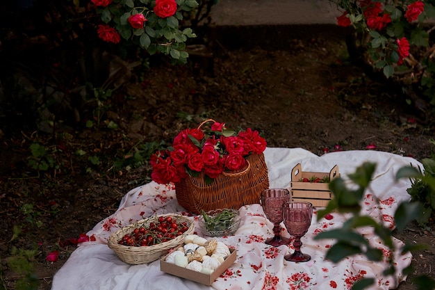 Picnic estivo estetico femminile con tovaglia marshmallow fragole bicchieri di vino tra rose rosa nel parco Serata romantica