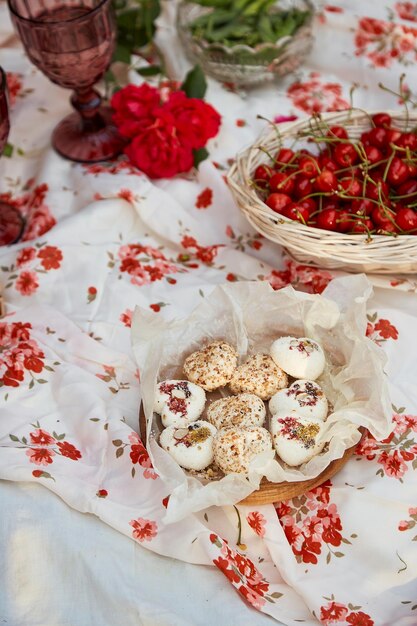 Picnic estivo estetico nel cortile soleggiato Tovaglia Scatola di marshmallow fragole ciliegie piselli e bicchieri di vino tra rose rosa Serata romantica apprezzamento del momento