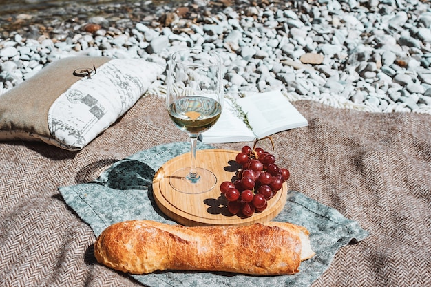 picnic estivo sulla costa con bicchiere di vino bianco baguette ciliegie uva cuscino libro aperto