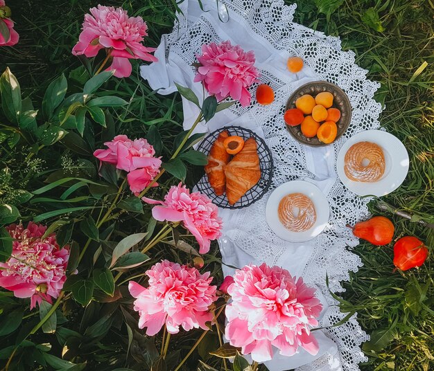 Picnic in stile vintage con peonie rosa, frutta e pane, luminosa giornata di sole, messa a fuoco selettiva