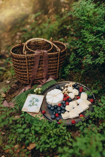 picnic nella foresta sullo sfondo di cespugli di muschio e mirtilli, formaggio e frutti di bosco su una lastra di metallo