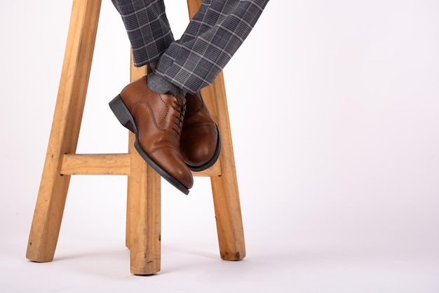 piede appeso a uno sgabello in legno con scarpe marroni su sfondo bianco