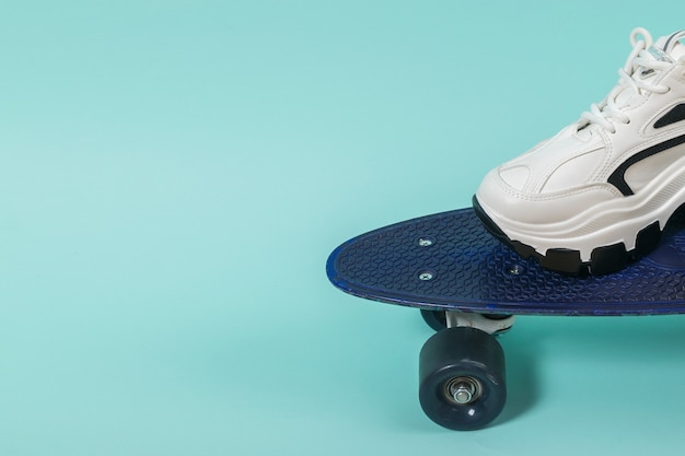 Piede in una scarpa da tennis bianca su uno skateboard blu. Stile sportivo.