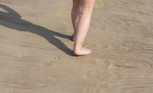 Piedi del bambino a piedi nudi che camminano sulla spiaggia di sabbia