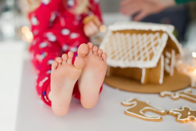 Piedi del bambino e casa di pan di zenzero di Natale Bambino seduto su un tavolo vicino a biscotti di Natale e casa di pan di zenzero