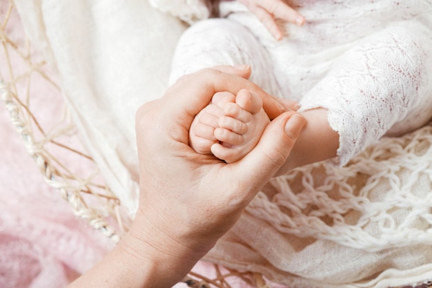 Piedi del neonato in mani della madre su fondo bianco.