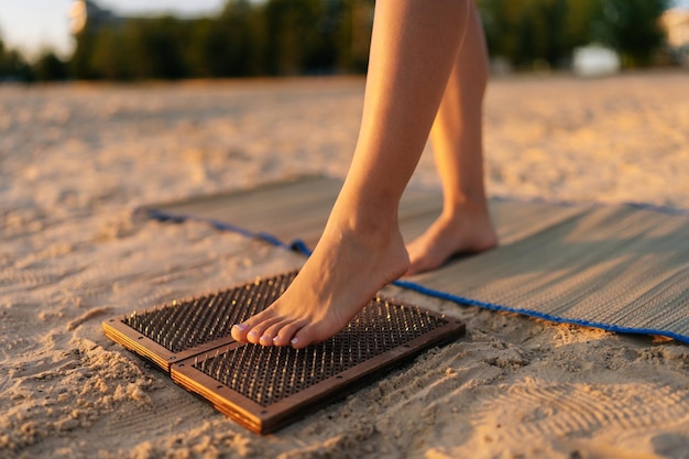 Piedi del primo piano di una donna irriconoscibile che calpesta la tavola Sadhu Nail durante la pratica della meditazione di concentrazione sulla spiaggia sabbiosa del mare al mattino di sole estivo