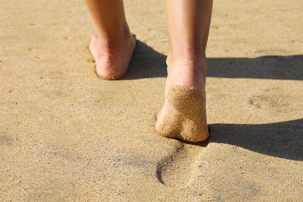 Piedi della donna che camminano sulla sabbia lasciando impronte
