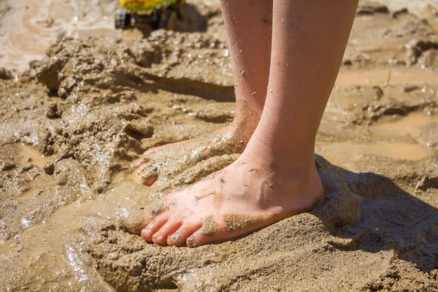 Piedi di bambini nella sabbia bagnata, fango. Bambino scalzo che gioca con la sabbia bagnata in una giornata di sole estivo.