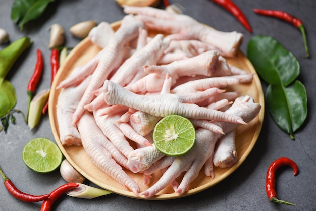 piedi di pollo su un piatto di legno con erbe e spezie limone peperoncino aglio foglie di lime kaffir, piedi di pollo crudi freschi per zuppa di cibi cotti sul tavolo scuro sullo sfondo della cucina