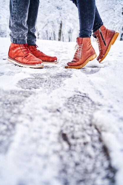 Piedi di una coppia su un marciapiede nevoso in stivali marroni