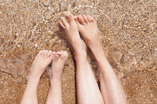 Piedi femminili e infantili sulla sabbia. riposo e aria di mare. vacanze di famiglia