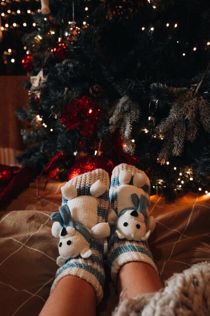 Piedi femminili in calzini accoglienti lavorati a maglia sullo sfondo dell'albero di Natale Atmosfera di Capodanno