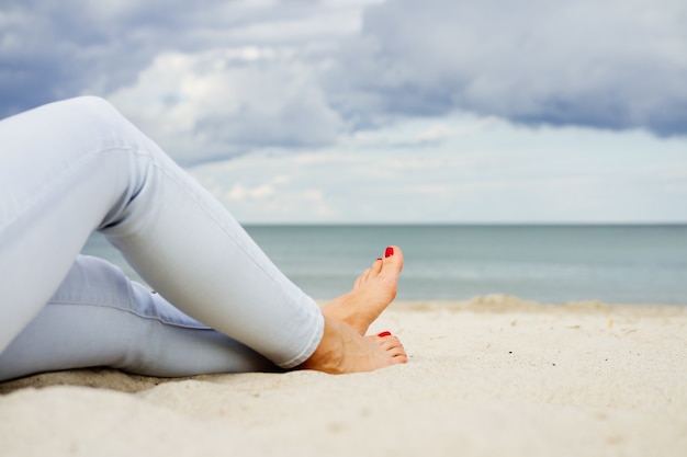 Piedi femminili in jeans sulla spiaggia di sabbia