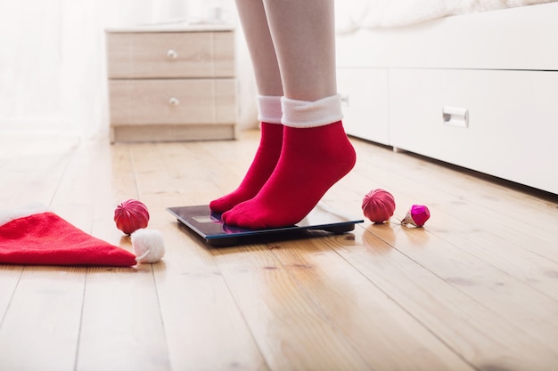 Piedi femminili in piedi su bilance elettroniche per il controllo del peso in calze rosse con decorazioni natalizie