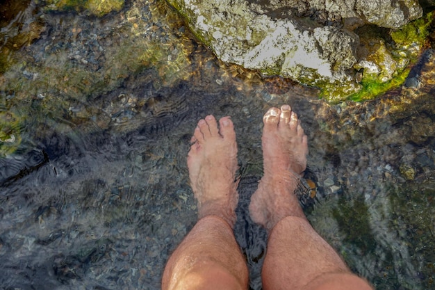 Piedi immersi nell'acqua limpida con piccole rocce di un fiume di montagna