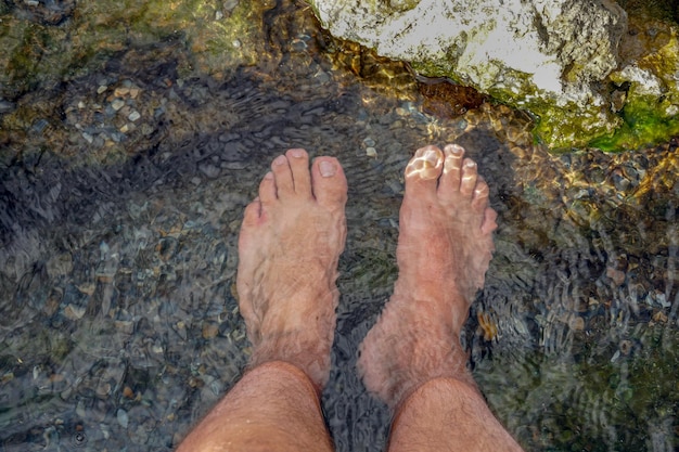 Piedi immersi nell'acqua limpida con piccole rocce di un fiume di montagna