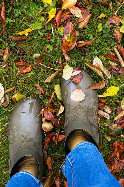 Piedi in stivali di gomma in piedi in erba bagnata con foglie cadute colorate Concetto di stile di vita a piedi in autunno