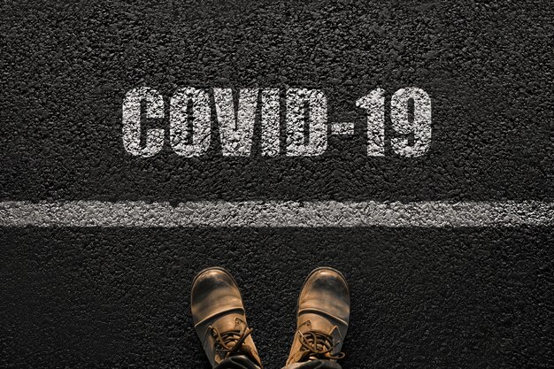Piedi maschili con stivali sull'asfalto con la scritta Covid-19. L'umanità e il concetto di virus. Coronavirus e viaggi