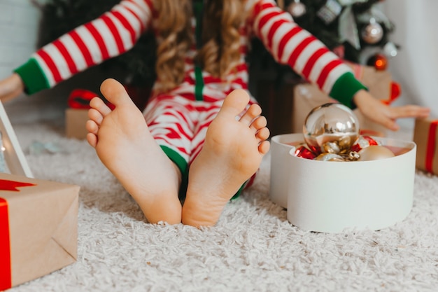 Piedi nudi di un bambino seduto sul pavimento vicino all'albero di Natale. Primo piano. Concetto di capodanno invernale. Natale