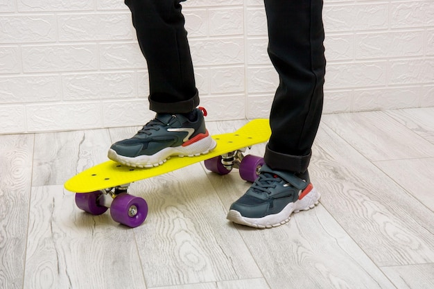 Piedi per bambini in scarpe da ginnastica in piedi su uno skateboard giallo