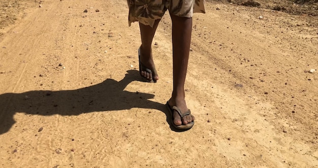 Piedi poveri del bambino che camminano su una strada sterrata in una calda giornata di sole.