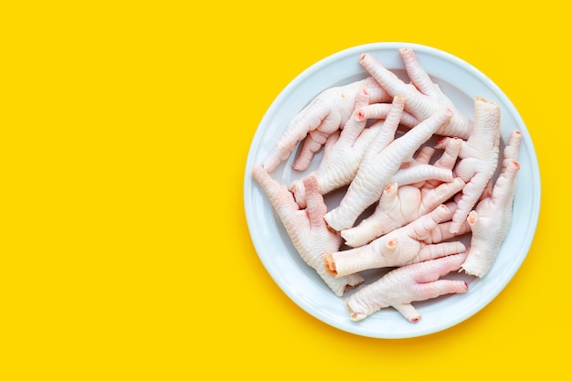 Piedini di pollo crudi in piatto bianco su fondo giallo.