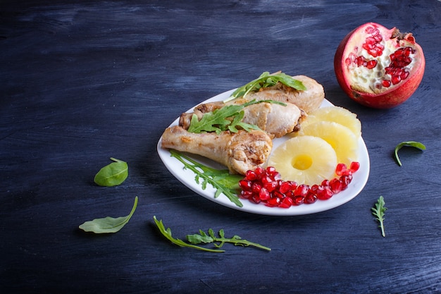 Piedini di pollo fritto con i semi della rucola, dell&#39;ananas e del melograno su fondo di legno nero.