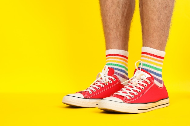 Piedini maschii in scarpe da ginnastica rosse e calzini LGBT su giallo