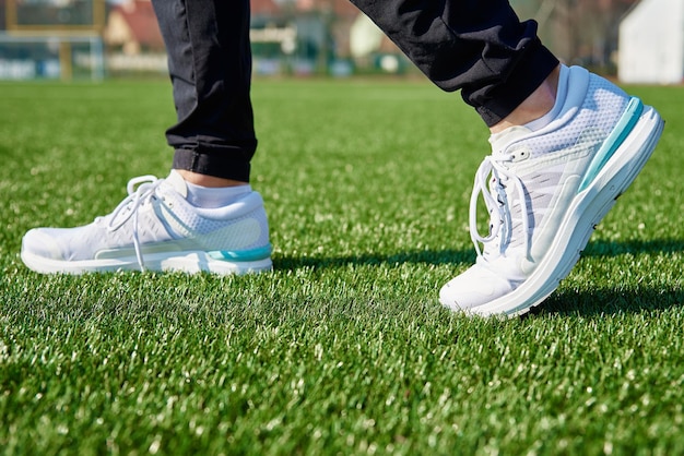 Piedini maschili con scarpe da ginnastica bianche allo stadio con erba verde primo piano Scarpe da ginnastica sportive per fare jogging Concetto di fitness e stile di vita sano