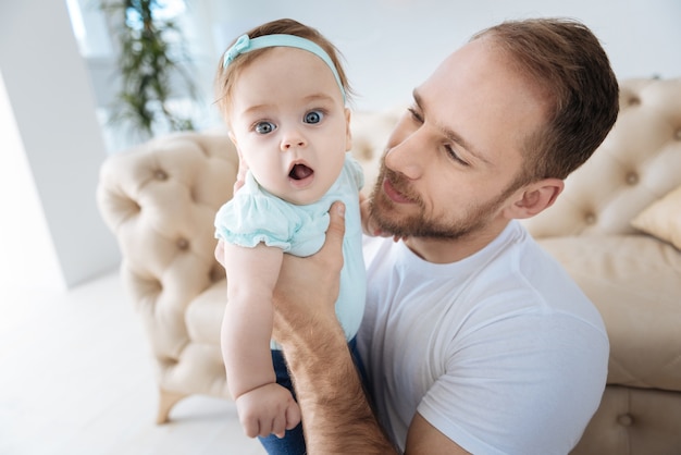 Pieno di emozioni felici. Divertente simpatico bambino piacevole in piedi vicino al suo giovane padre e distogliere lo sguardo mentre esprime interesse e positività