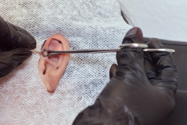 Piercing su un orecchio Conch e piercing ad elica si chiudono Professionista che tiene il gioiello