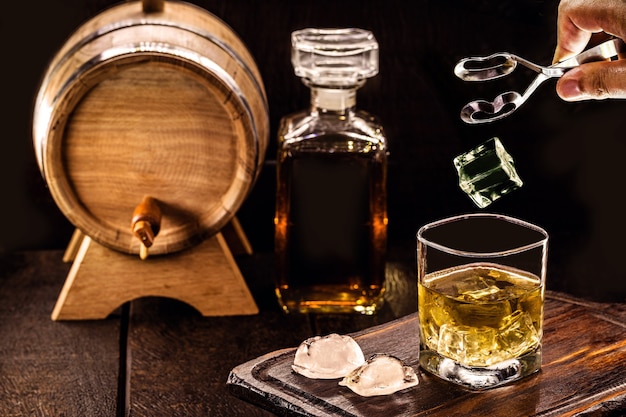 pietra di ghiaccio che cade nel bicchiere di whisky invecchiato, spazio per il testo, sfondo del pub