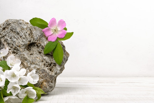 Pietra naturale con fiori bianchi e rosa su un tavolo di legno bianco