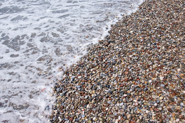 Pietre di ghiaia sulla spiaggia del mare. Le onde ondeggianti del mare con schiuma