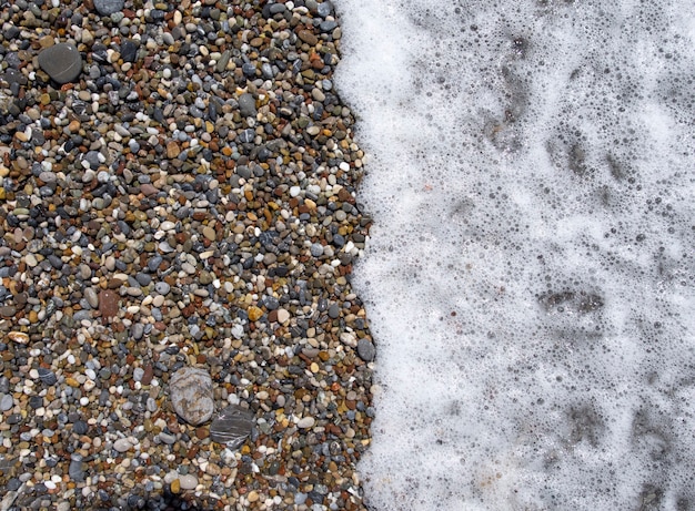 Pietre di ghiaia sulla spiaggia del mare. Le onde ondeggianti del mare con schiuma