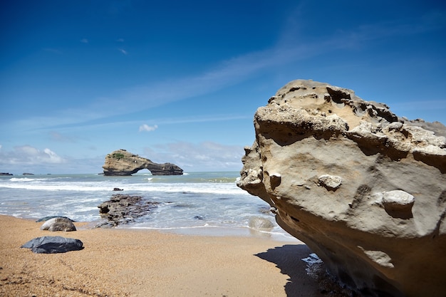 Pietre su una spiaggia sabbiosa e un'isola rocciosa. Costa atlantica nel sud-ovest della Francia. Giornata di sole estivo con cielo blu