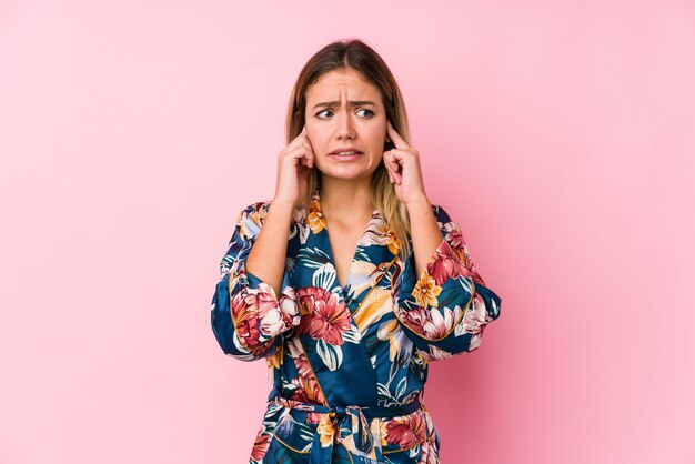 Pigiama da portare della giovane donna caucasica che copre le orecchie con le mani.