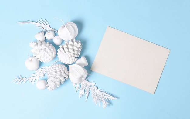 Pigne di colore bianco, rami, fiori physalis e con carta regalo vuota. Piatto minimo concetto. Oggetti bianchi su sfondo blu.