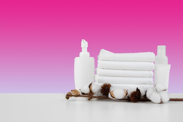 Pila di asciugamani bianchi e bottiglie di prodotti per la cura della pelle sul tavolo bianco