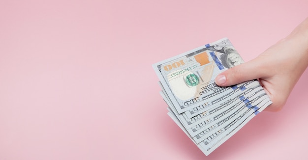 Pila di banconote in dollari in mano femminile su sfondo rosa
